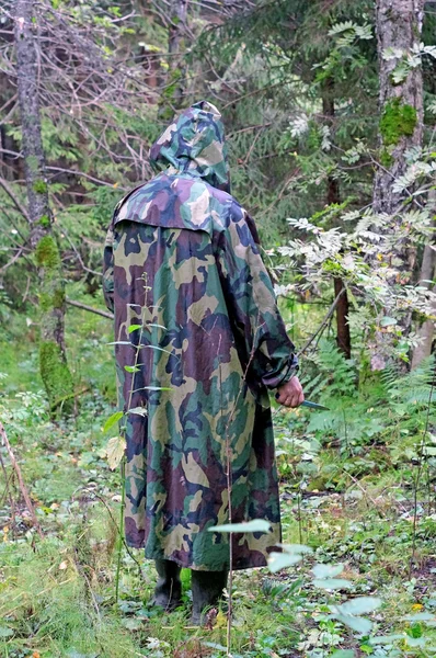 A man in a camouflage hooded standing back in the woods with a k