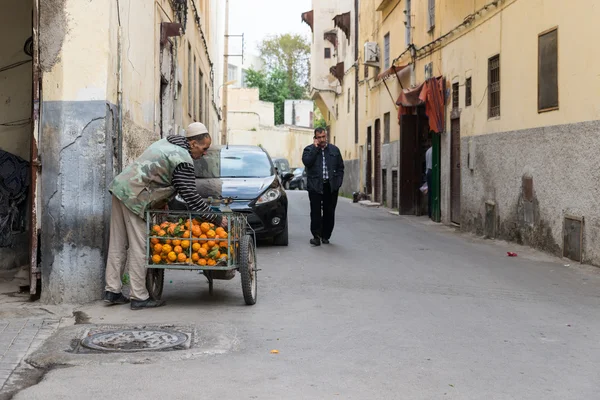 One man sells orange while another man talks to the mobile phone