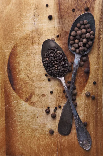 Image of spoons full of black peppercorn and allspice on wooden