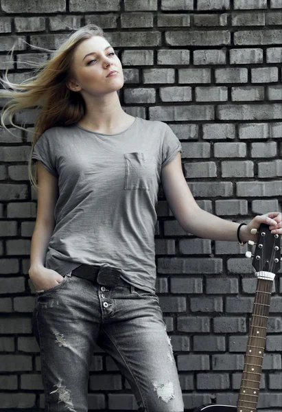 Portrait of a woman with a guitar near brick wall