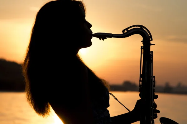 Portrait of a woman in a dress playing the saxophone near the river