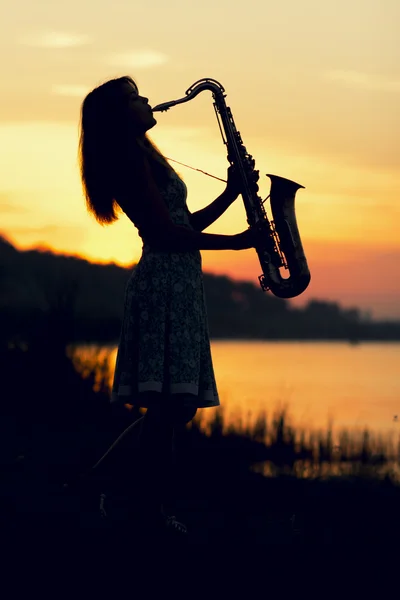 Silhouette of a young woman playing a wind instrument at dawn on the river