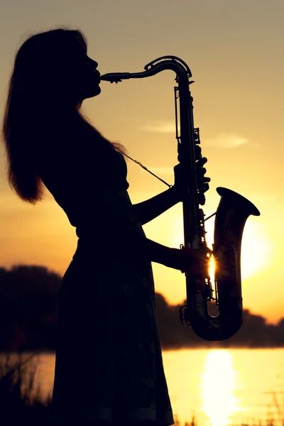 Portrait of a woman in a dress playing the saxophone near the river