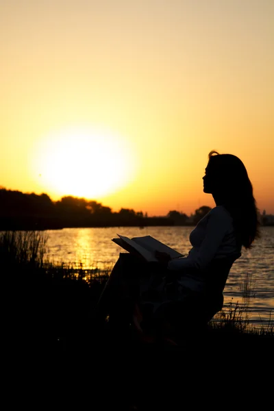 Outlines of a beautiful young woman with a book by the river at dawn of the day