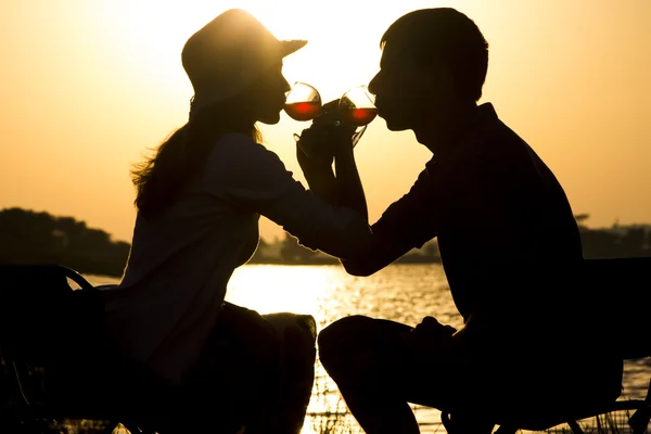 Silhouette of a young couple in love to leave on a picnic out of town drinking wine brotherhood of glass goblets