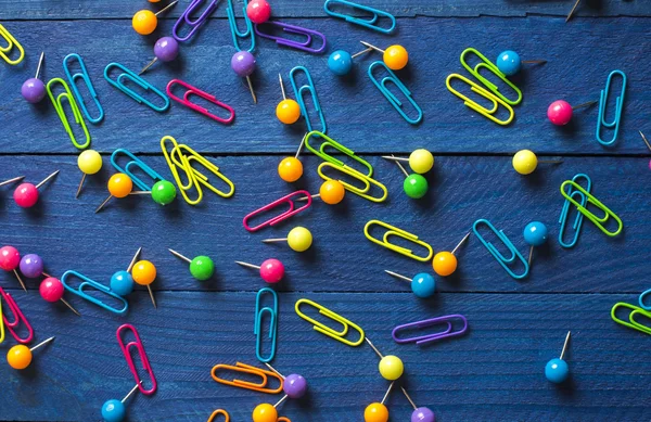 Background of scattered colored round pins and paper clips on a table