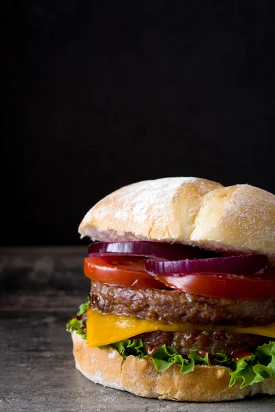 Delicious burger with cheddar cheese, tomato, lettuce and onion. Black background