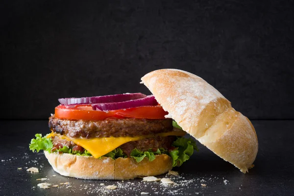 Delicious burger with cheddar cheese, tomato, lettuce and onion. Black background