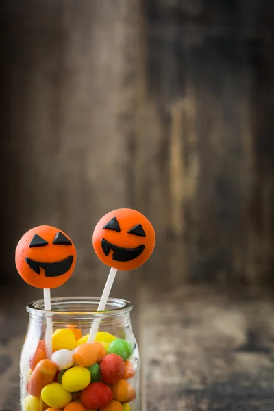 Halloween cake pops and colored candies on rustic wood background