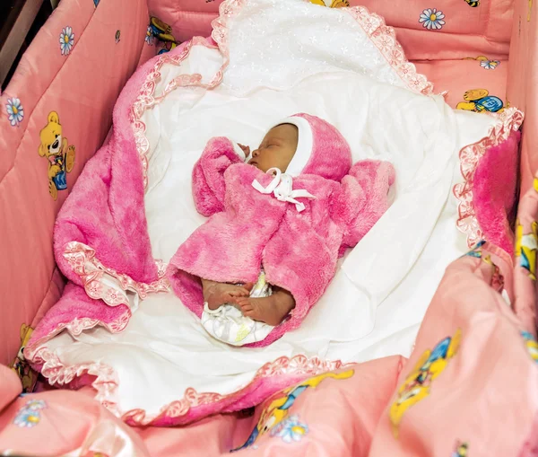 A newborn baby in pink clothes sleeps in a crib