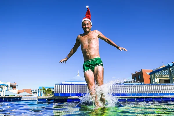 A man in a Santa Claus Cap jumps into a pool at a tropical resor