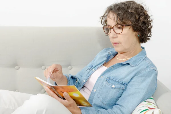Woman of middle age reads, sitting on the sofa