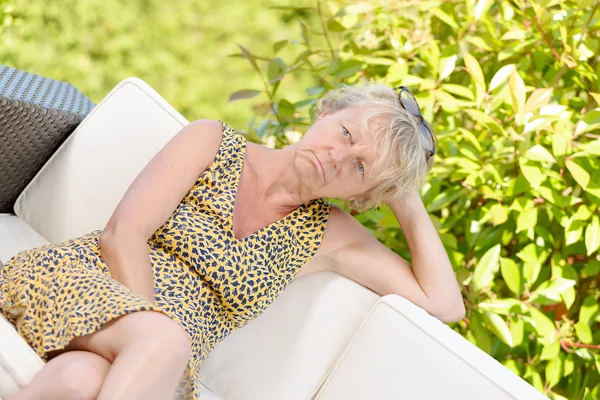 Smiling blonde woman sitting on the sofa , in a garden