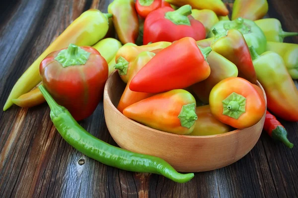 Red, green, orange pepper of different grades in a wooden bowl o