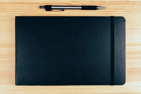 Blank black diary cover and pen on wooden table, mock up