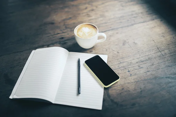 Open blank notebook, pen, cell phone and cup of coffee on wooden
