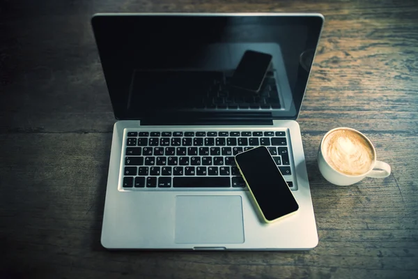 Blank cell phone and laptop on a wooden table with cup of coffee