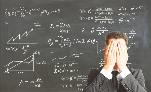 Stressed businessman covering face with palms on chalkboard background with mathematical formulas. Education concept