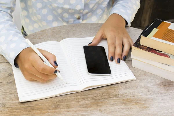 Girl writes in notebook with cell phone