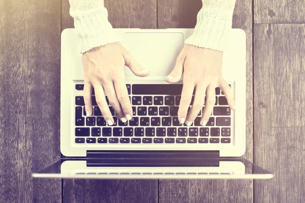 Girl hands typing on laptop on a wooden table