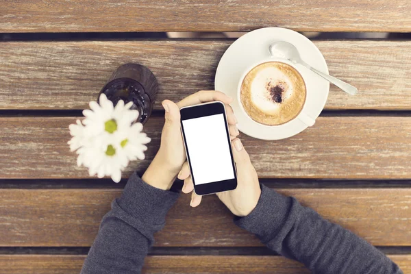Girl hands with blank smartphone, cup of coffee and flowers on a