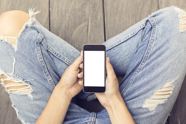 Girl in jeans with blank smartphone on the wooden floor, mock up