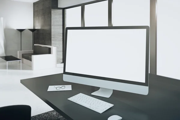 Blank white computer screen on wooden table in modern office, mo