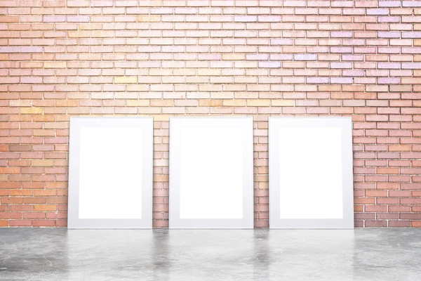 Blank white picture frames on concrete floor and red brick wall,