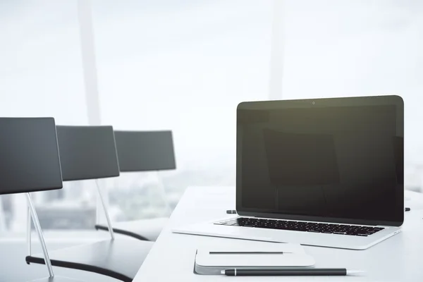 Blank black laptop screen on white table in conference room with