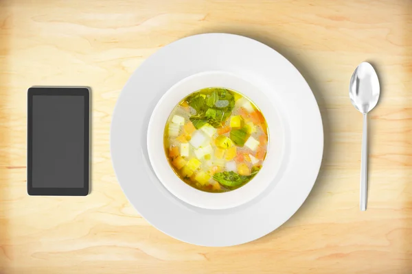 Minestrone soup with cell phone and sppon on wooden table