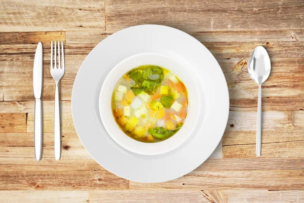 Minestrone soup in white plate with knife, fork and spoon on woo