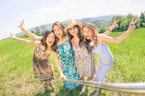 Multiracial girlfriends taking selfie with stick at country picnic - Happy friendship concept and fun with young people having fun together - Sunny afternoon warm color tones and tilted horizon