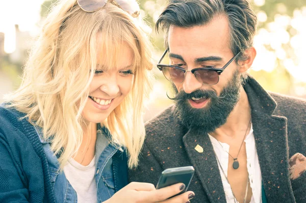Happy young couple with vintage clothes having fun with smartphone - Beginning of love story with hipster best friends on mobile phone - Addiction concept with new technology - Shallow depth of field