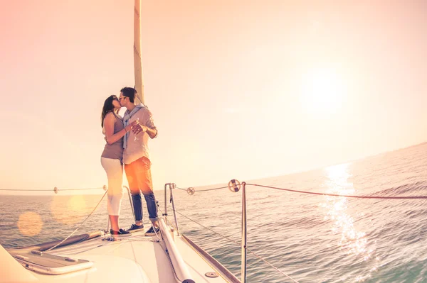 Rich young couple in love on sailboat cheering at sunset - Happy wander lifestyle concept sailing around world - Soft focus on rose quartz filter - Lens flare and tilted horizon as part of composition