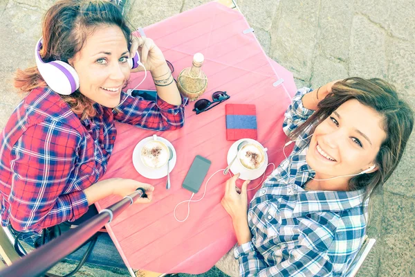 Top view of hipster girlfriends taking selfie with stick - Female friendship concept with girls drinking cappuccino at coffee bar restaurant - Best friends having fun together - Rose quartz color tone