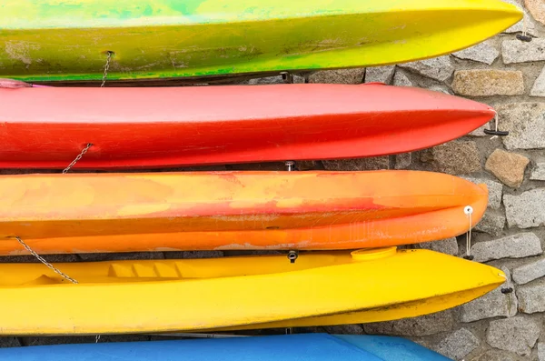 Row of multicolored kayaks against stonewall background - Summer travel and wanderlust concept with vivid colored water sport equipment