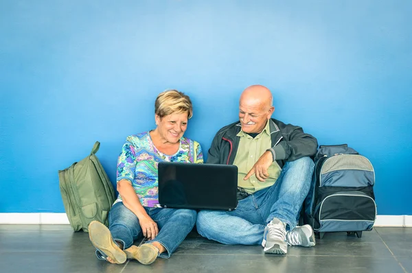 Happy senior couple sitting on the floor with laptop waiting for a flight at the airport - Concept of active elderly and interaction with new technologies - Travel lifestyle without age limitation