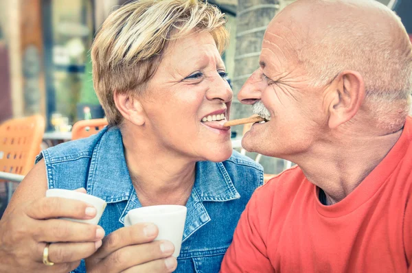 Happy playful senior couple in love tenderly enjoying a cup of coffee - Joyful elderly active lifestyle - Man having fun and smiling with her wife in a bar cafe restaurant during vacation