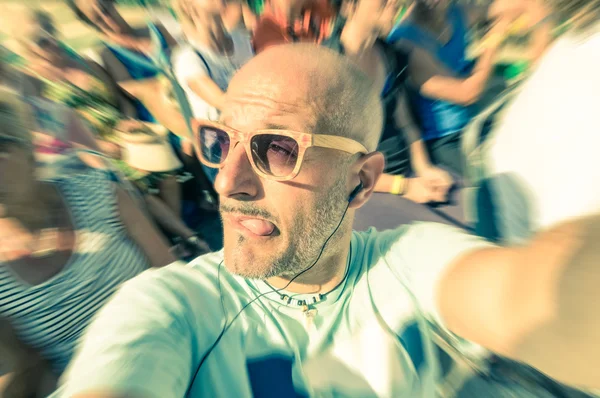 Bald funny man taking a selfie in the crowd with stupid tongue out expression - Travel lifestyle enjoying moment of carefree loneliness - Vintage filtered look