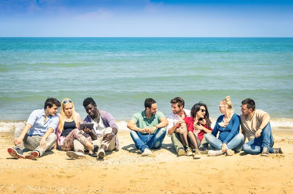 Group of international best friends sitting at beach talking with each other - Concept of multi cultural friendship against racism - Interaction with new technologies tablet and contact with nature