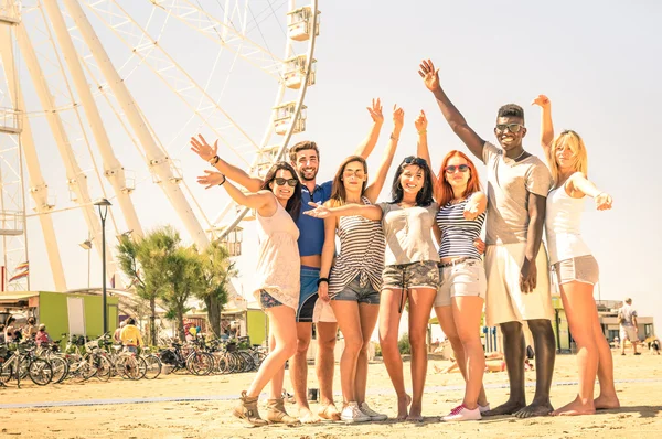 Group of multiracial happy friends cheering at ferris wheel - International concept of happiness and multi ethnic friendship all together against racism for peace and fun - Warm nostalgic filter