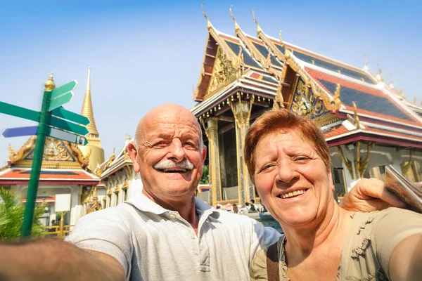 Senior happy couple taking a selfie at Grand Palace temples in Bangkok - Thailand adventure travel to asian destinations - Concept of active elderly and fun around the world with new technologies