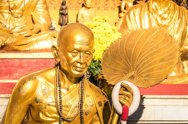 Golden statue of old buddhist monk with flowers ring in the sanctuary of Doi Suthep - Ancient buddha temple in Chiang Mai province in Thailand - Concept of faith and religion in asian countries