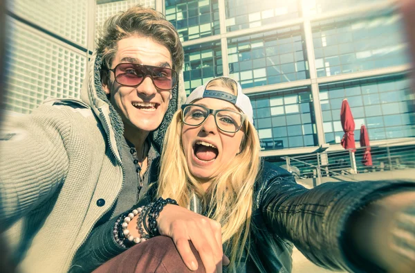 Young hipster couple in love taking a funny selfie in urban city background - Alternative concept of fun and interaction with new trends and technology - Vintage filtered look with blurred edges