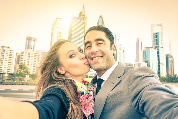 Young hipster couple in love taking a selfie at Dubai city skyline - Concept of fun and interaction with new trends and technology - Vintage filtered look with sun flare and soft focus on the faces