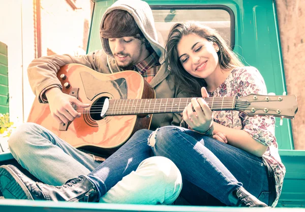 Romantic couple of lovers playing guitar on old fashioned mini car - Nostalgic retro concept of love with soft focus on the faces of boyfriend and girlfriend - Overexposed desaturated vintage filter