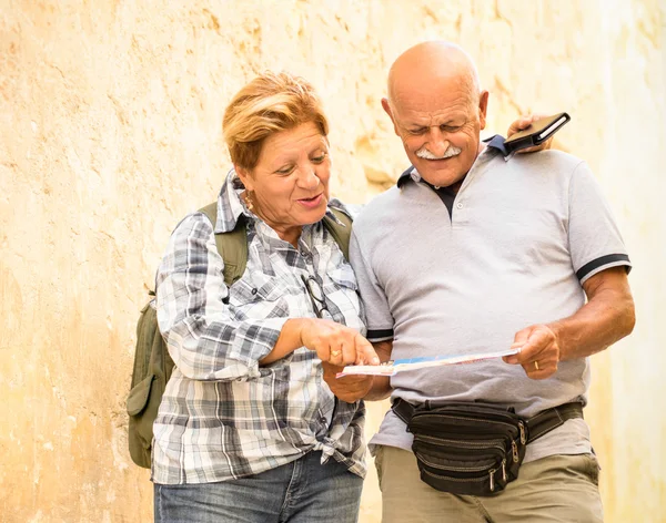 Active senior couple exploring old town of La Valletta with travel map - Concept of youthful elderly and tourist retired lifestyle without age limitation - Warm neutral color tones in cloudy shadow