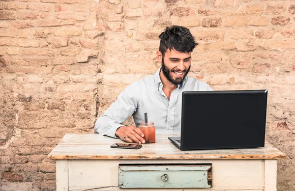 Young hipster guy with mustache sitting at vintage desk with laptop computer in grunge alternative office - Concept of start up business enjoying working hours - Soft retro desaturated filtered look