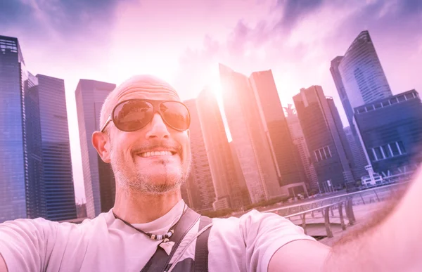 Handsome man taking selfie at modern urban area of Marina Bay in Singapore at sunset - Adventure travel lifestyle around south east Asia - Composition with tilted horizon and blue marsala color tones