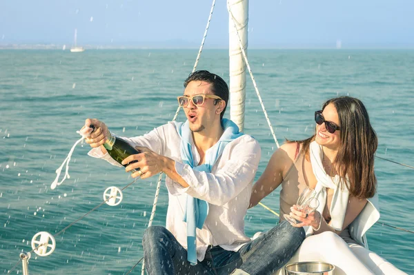 Young couple in love on sailing boat cheering with champagne wine bottle - Happy girlfriend birthday party cruise travel on luxury sailboat - Focus on boyfriend face with sunny afternoon color tones